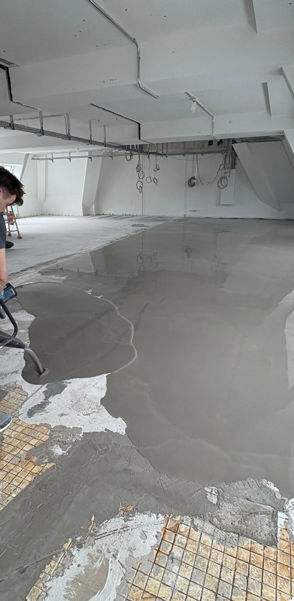 Arbeiter trägt Nivelliermasse auf Betonboden auf zur Untergrund vorbereiten in großzügigem Innenraum