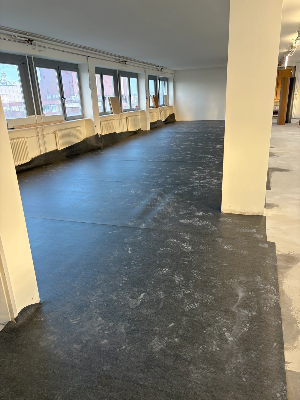 Helle Gewerbefläche mit großen Fensterfronten und frisch verlegtem schwarzen Kautschukboden