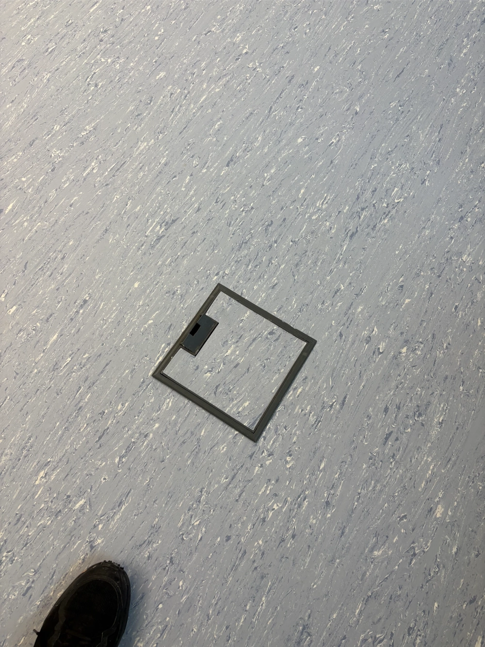 Offener Bodenausschnitt mit herausgenommener Abdeckung auf hellem, grauem Bodenbelag