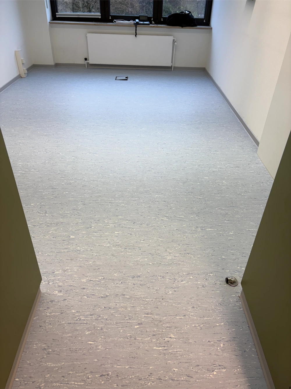 Leerstehender Raum mit frisch verlegtem hellgrauen PVC Boden und Sockelleisten