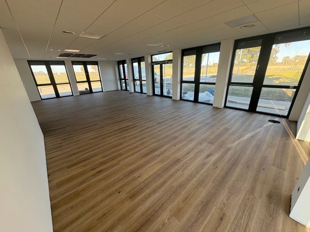 Großer leerer Raum mit frisch verlegtem Laminatboden und bodentiefen Fenstern – Laminat verlegen