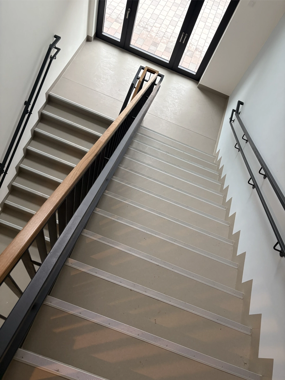 Gewerbliche Bodenarbeiten im Treppenhaus mit neu verlegtem grauen Bodenbelag, Metall-Anti-Rutschstreifen und schwarzen Handläufen