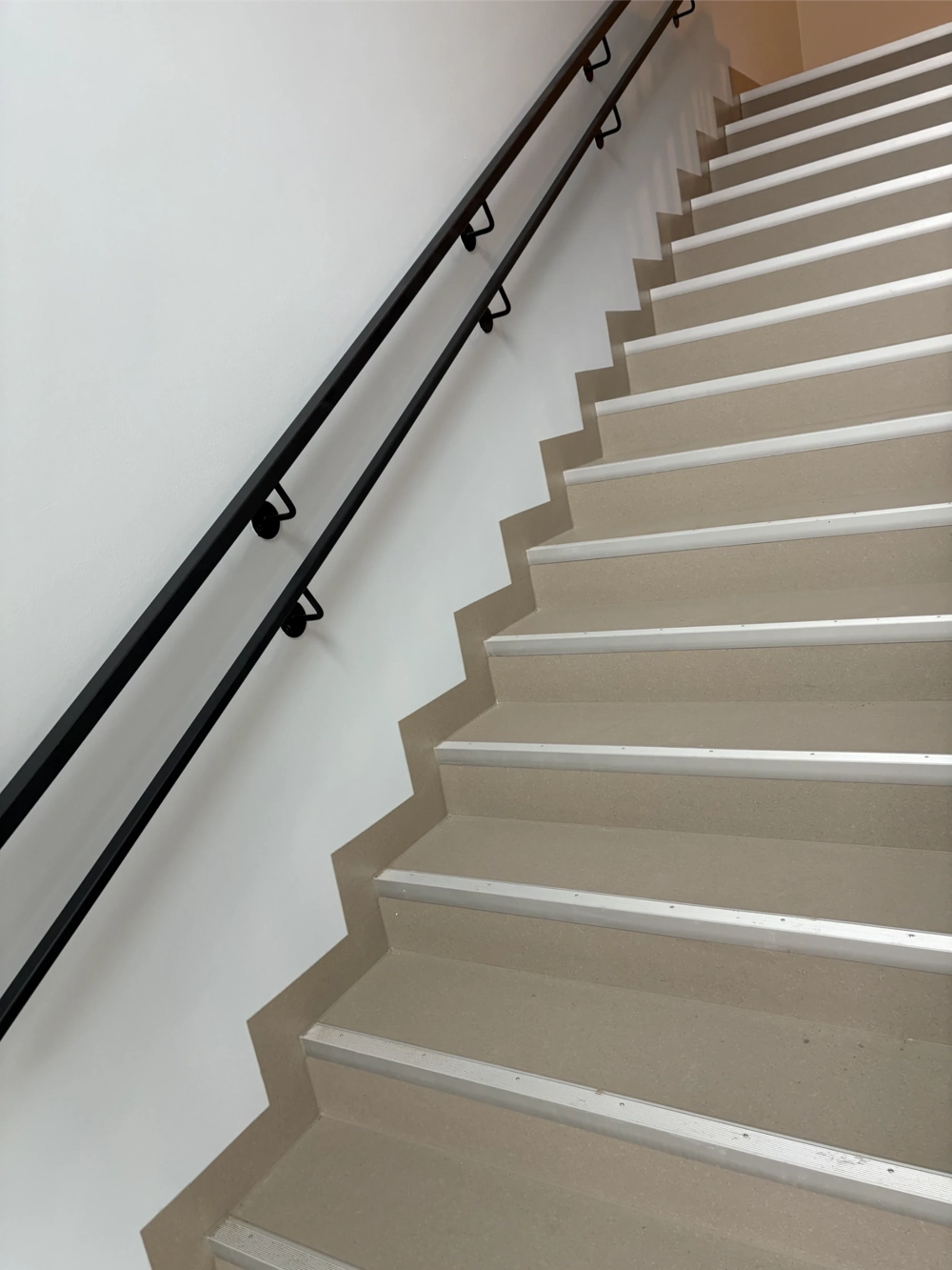 PVC Boden verlegen: Beigefarbener Treppenhausbelag mit weißen Stufenkanten und schwarzem Handlauf