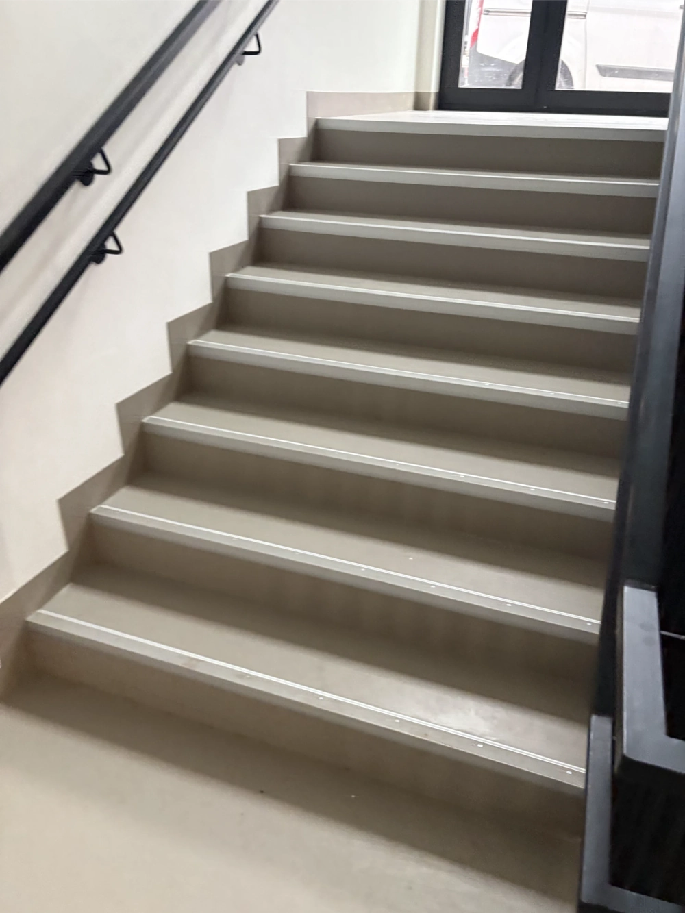 Hellgraue Innentreppe mit neuem Bodenbelag und schwarzen Handläufen – Boden Renovierung