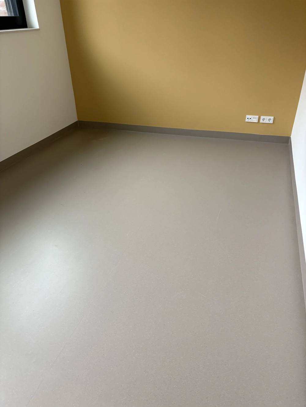 Raum mit frisch verlegtem grauen Vinylboden, sauberer Sockelleiste und Wandsteckdosen, Vinylboden verlegen