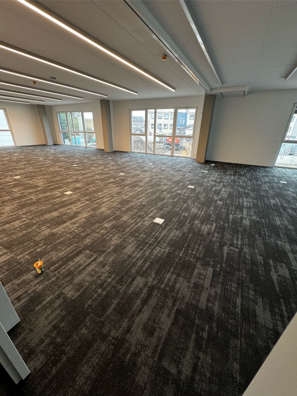 Leerer Büroraum mit neu verlegtem dunkelgrauen Teppichboden und LED-Deckenbeleuchtung, Teppich verlegen