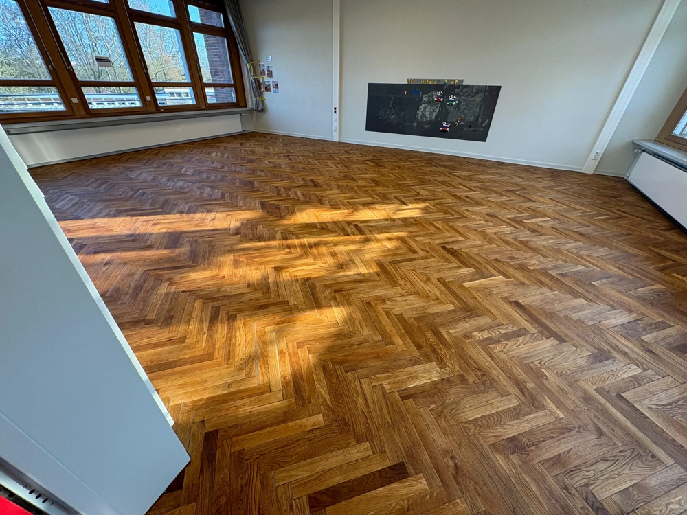 Leerstehender Raum mit frisch verlegtem Fischgrät-Parkettboden in warmem Holzton und hellem Tageslicht