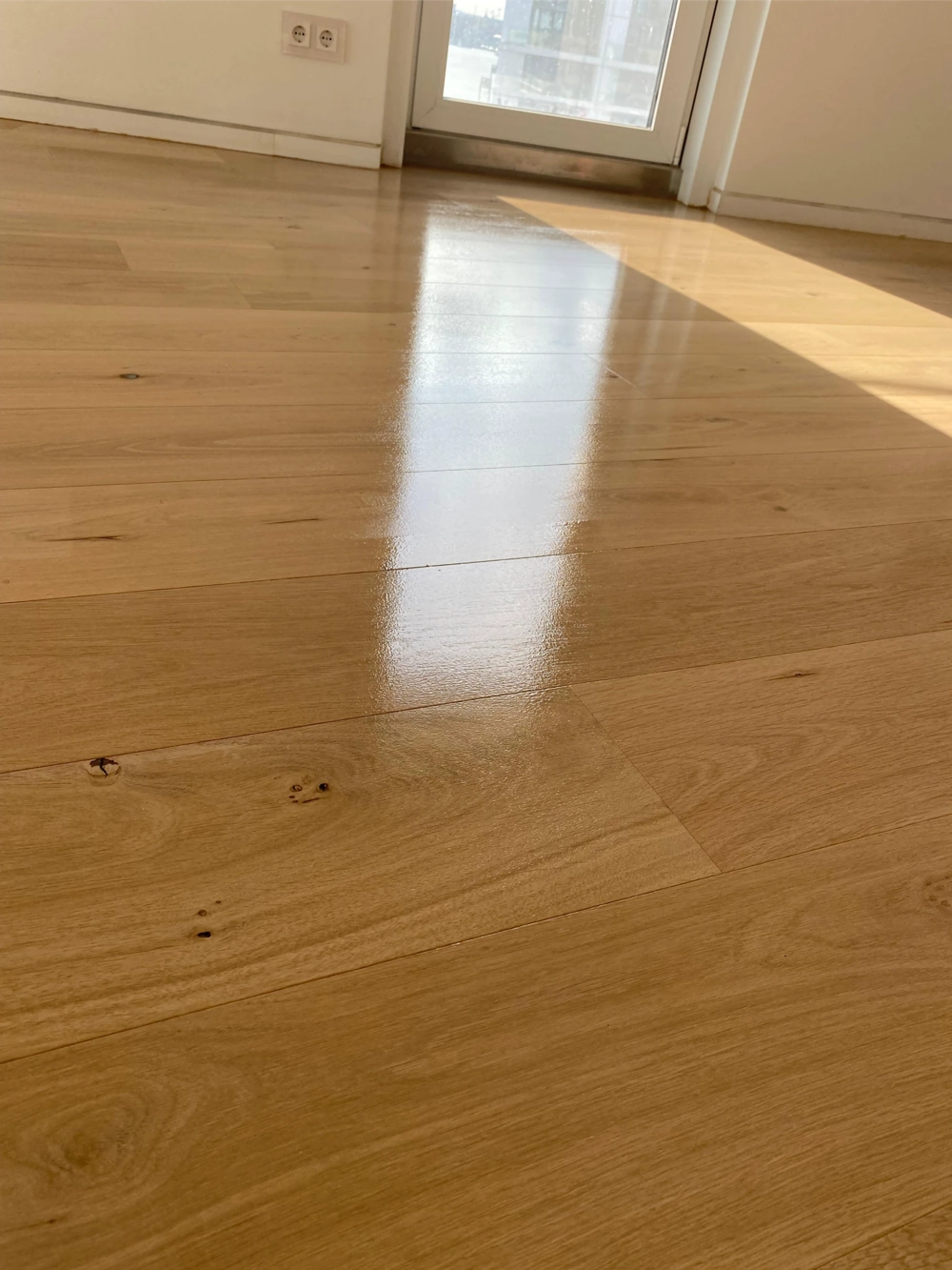 Nahaufnahme frisch verlegter Eichenparkettböden in hellem Wohnraum mit Fensterlicht