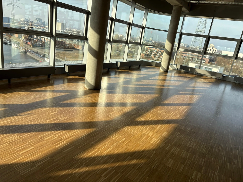 Offener Raum mit frisch verlegtem Parkettboden und bodentiefen Fenstern Parkett verlegen