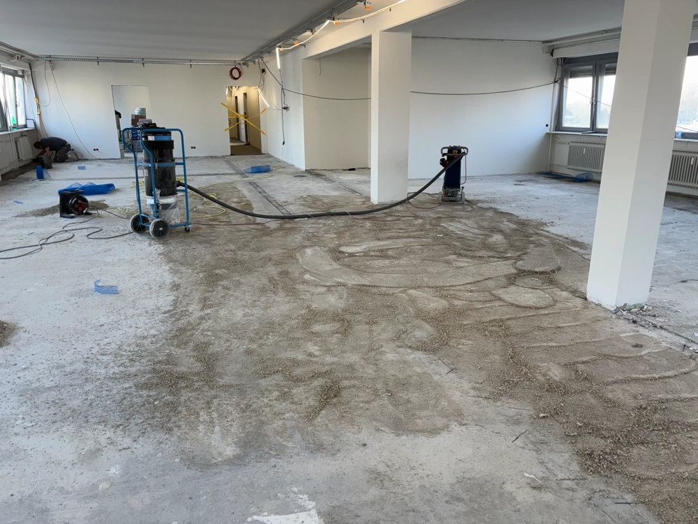 Großer Raum mit freigelegtem Estrich und Maschinen zum Untergrund vorbereiten