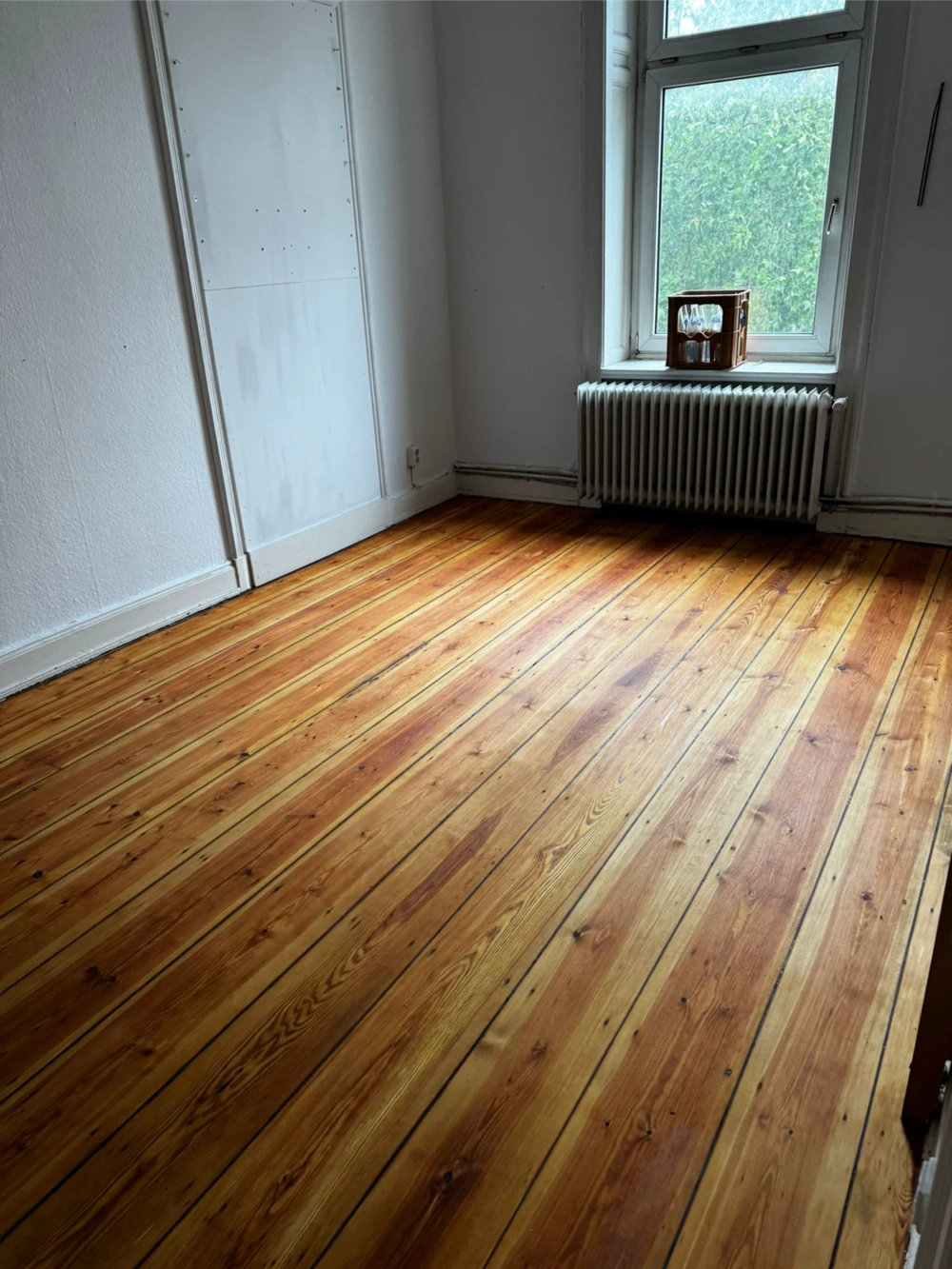 Geschliffenes Dielenparkett nach Parkett schleifen in hellem, leerem Raum mit Fenster und Heizkörper