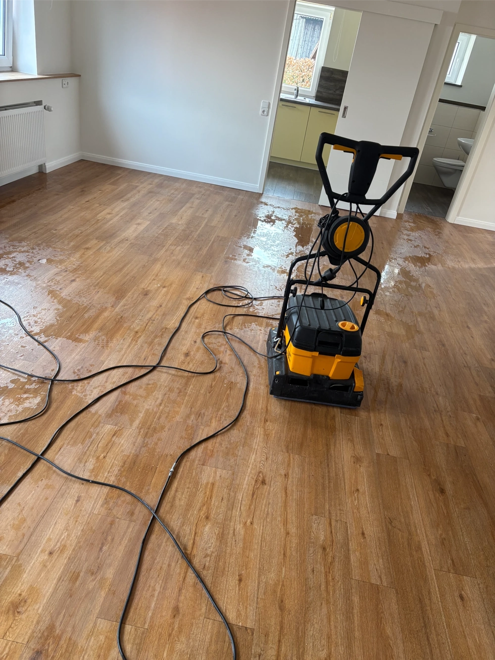 Bodenschleifmaschine auf feuchtem Holzboden in hellem Raum beim Parkett schleifen