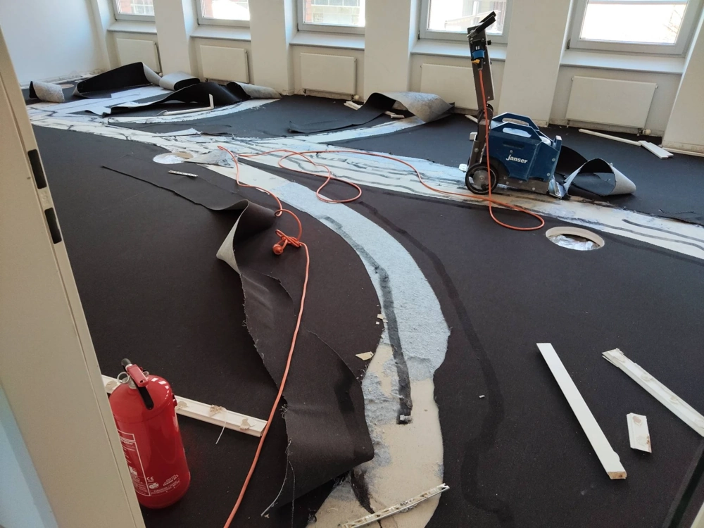 Losgelöste Teppichbahnen und Bodenabtragsmaschine beim Teppich entfernen in einem Büro