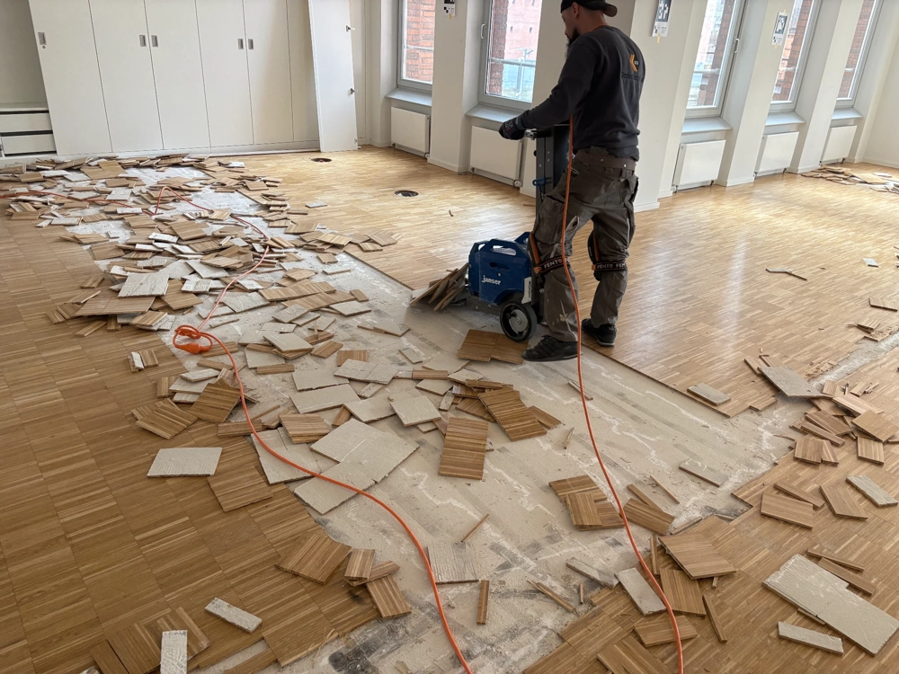 Handwerker beim Parkett entfernen mit Spezialmaschine in großem, hellem Raum