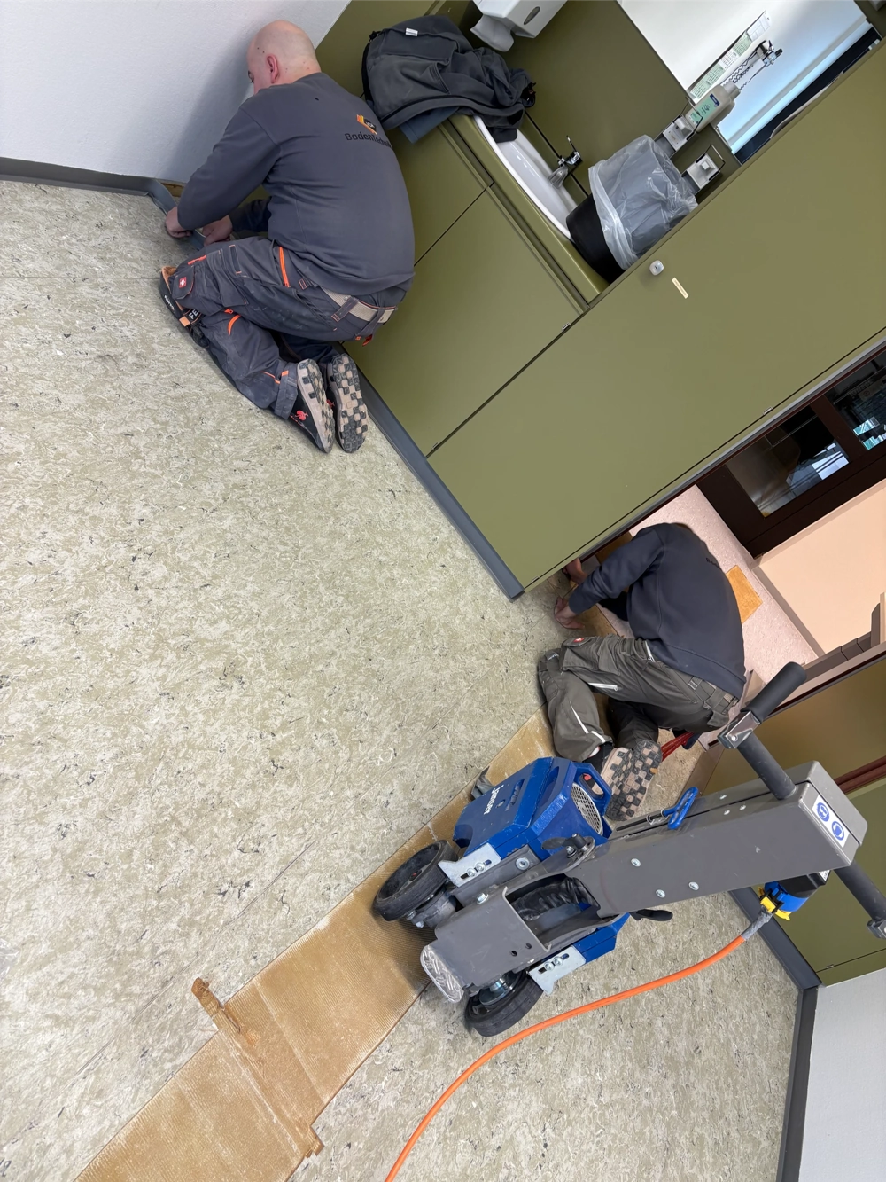 Zwei Handwerker beim PVC Boden entfernen unter einer Schrankzeile