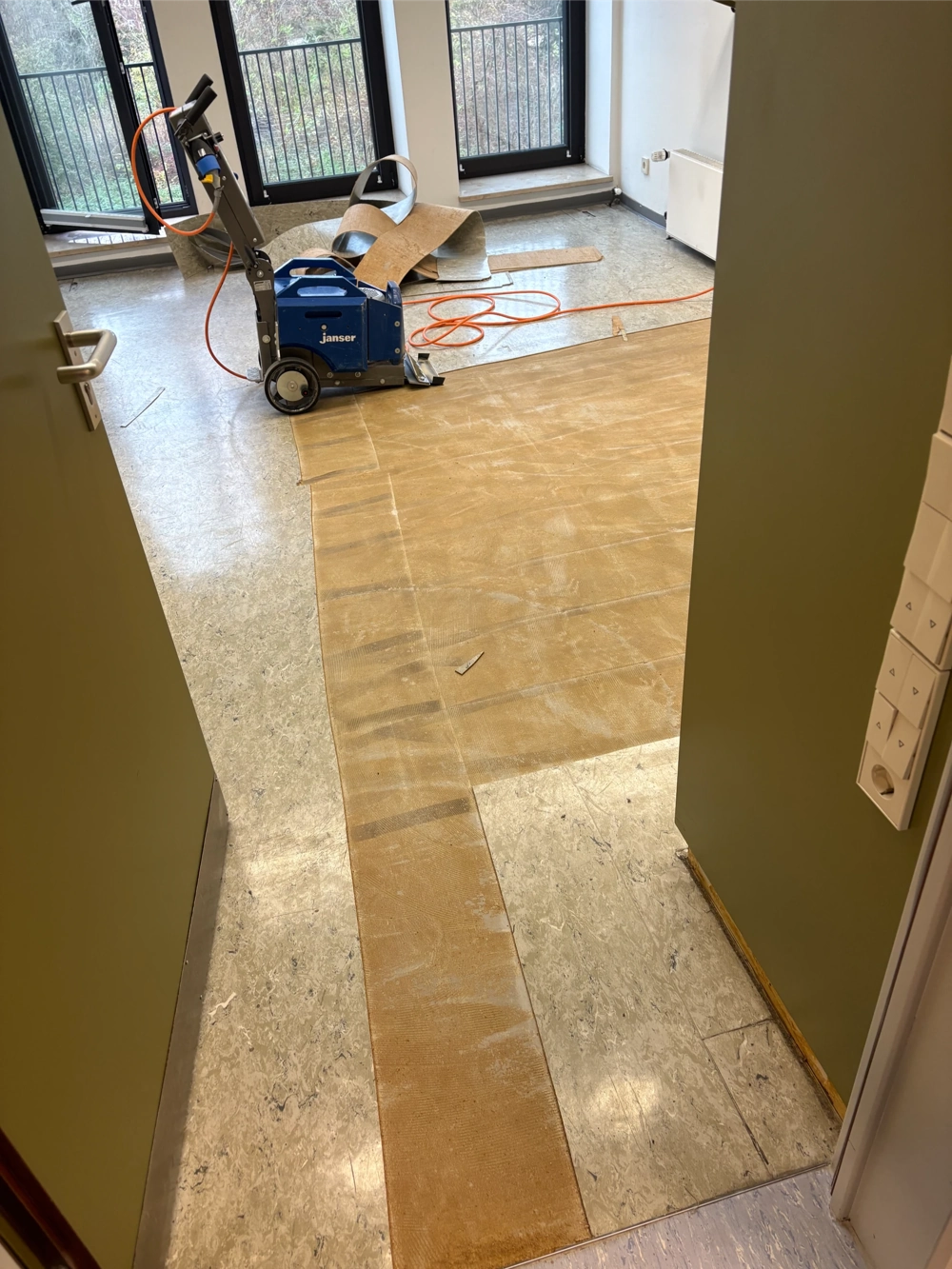 Offener Raum mit Profi-Maschine und Schlauch beim Linoleum entfernen, teilweise abgezogener Bodenbelag sichtbar