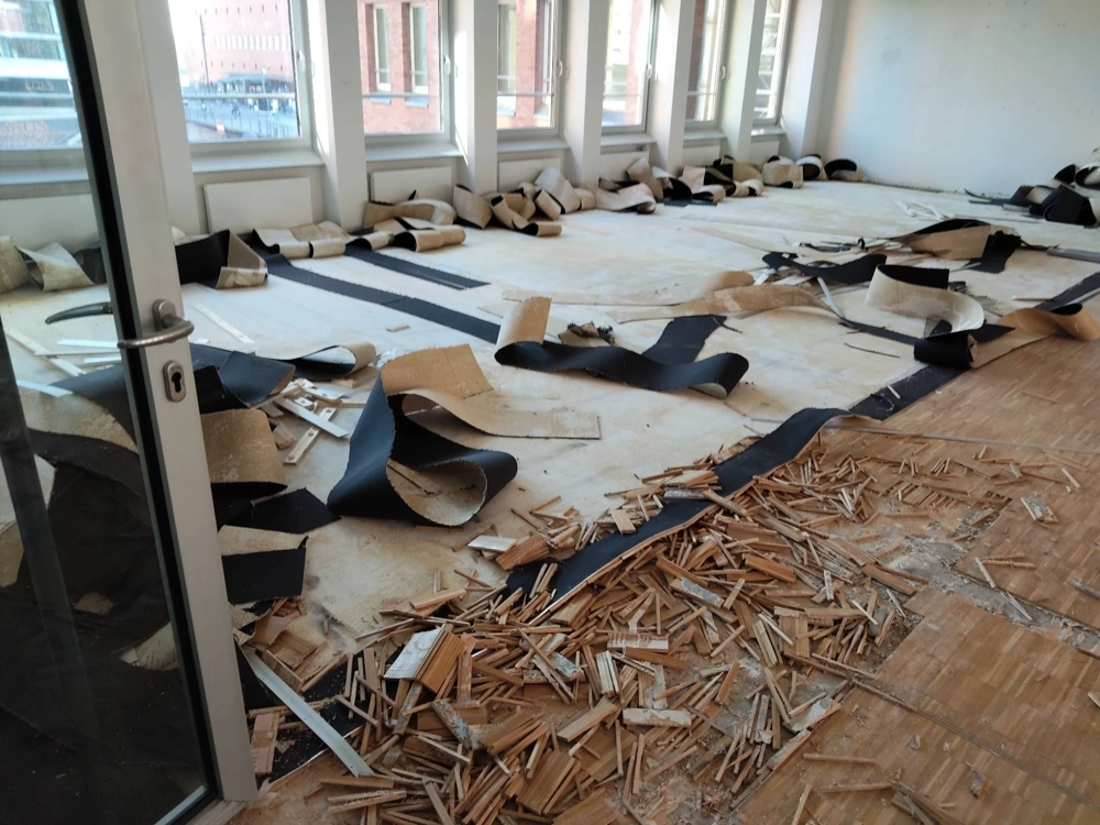 Großzügiger Raum mit freigelegtem Untergrund und Holzabfällen beim Parkett entfernen