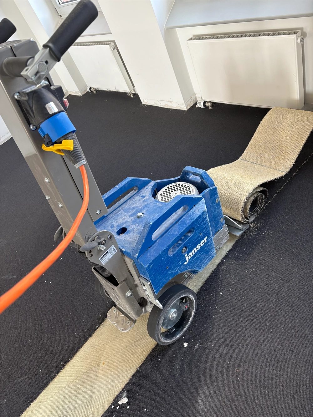 Mobile Maschine zum Teppich entfernen auf schwarzem Untergrund, aufgewickelter Teppich im Vordergrund