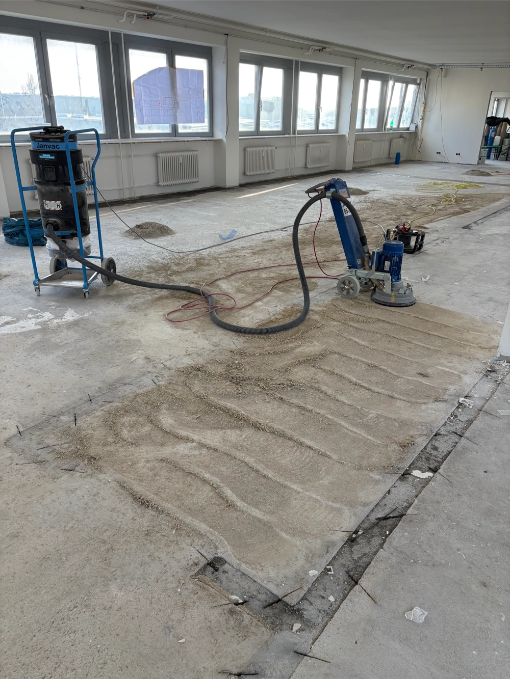 Leerer Raum mit Bodenschleifmaschine und Staubabsaugung für Untergrund vorbereiten