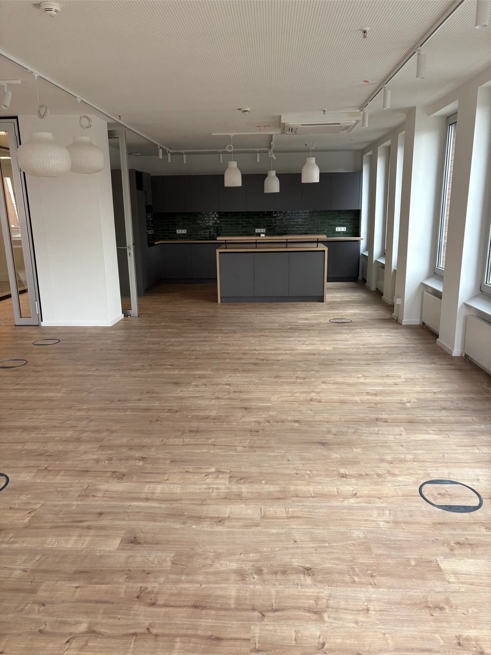 Heller Raum mit raumhohen Fenstern und frisch verlegtem Laminatboden vor zeitloser Küchenzeile – Laminat verlegen