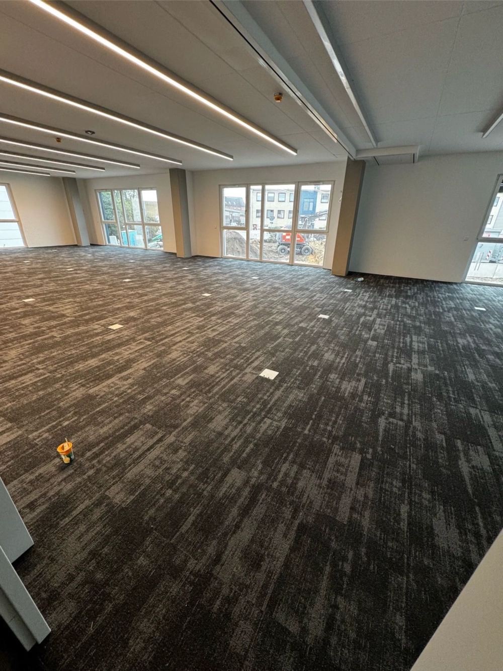 Große, helle Bürofläche mit neu verlegtem dunkelgrauen Teppichbelag unter integrierter Deckenbeleuchtung – Teppich verlegen